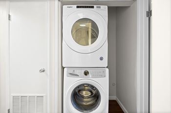 A white front load washing machine is stacked on top of a smaller dryer in a small laundry room.